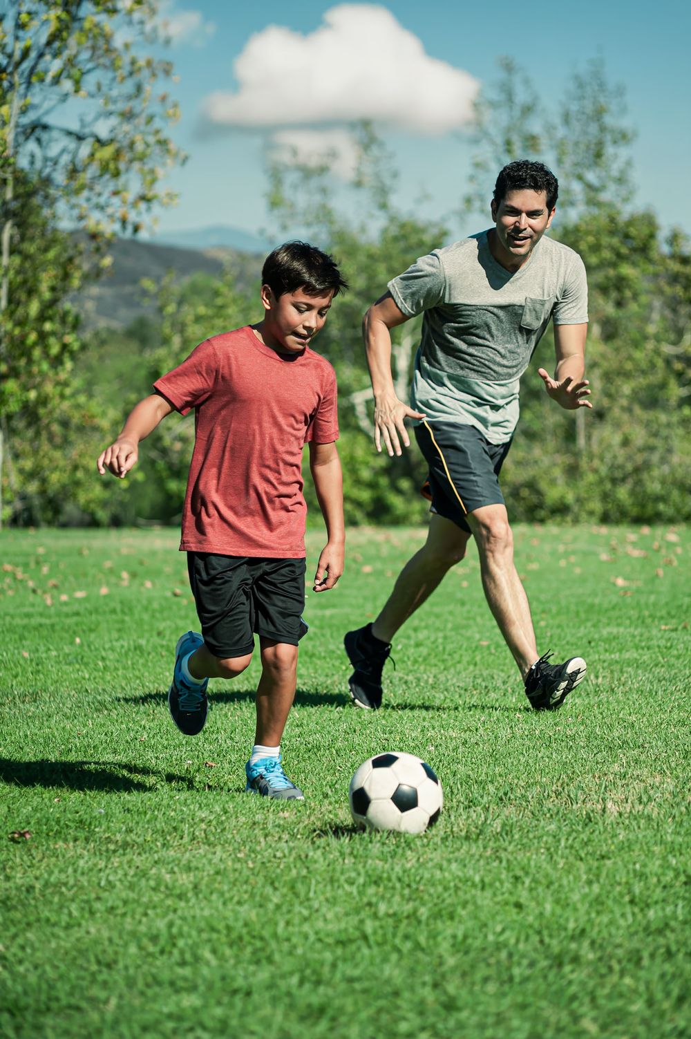 A man and boy play soccer together on a lush green field on a sunny day.