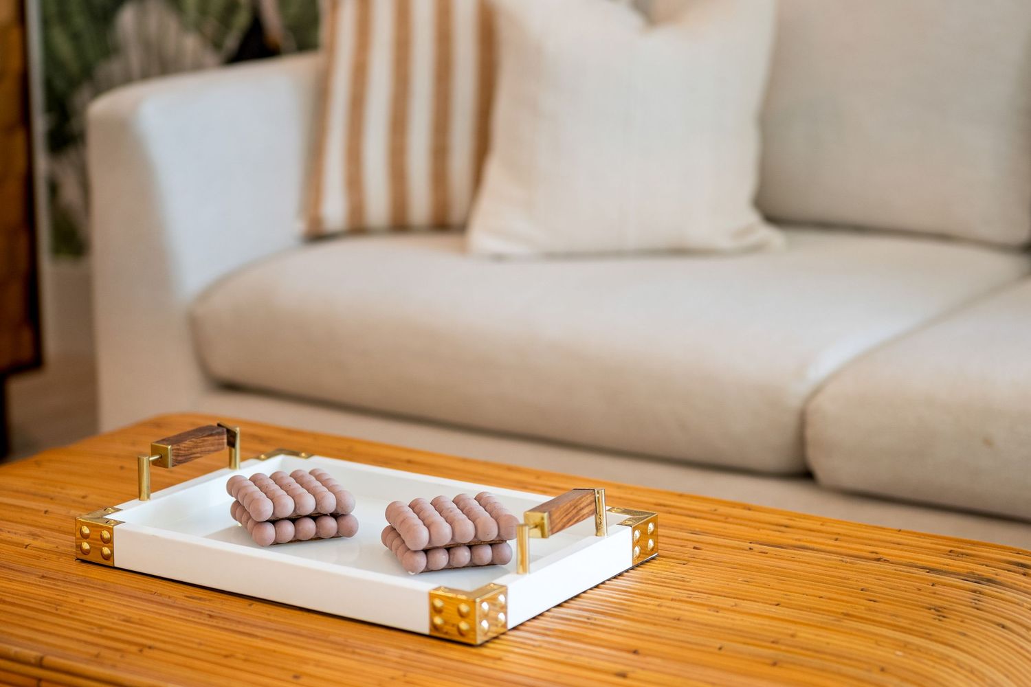A modern living room coffee table with wooden tray holding chocolate snacks and neutral couch in the background.