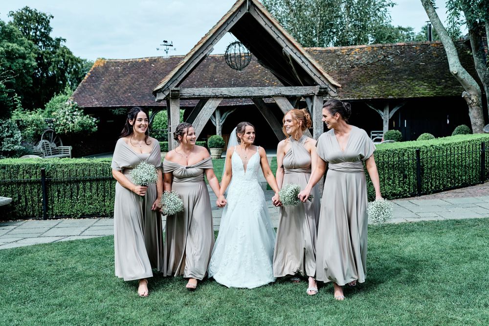 Wedding party poses outside rustic venue with bridesmaids in matching grey dresses.