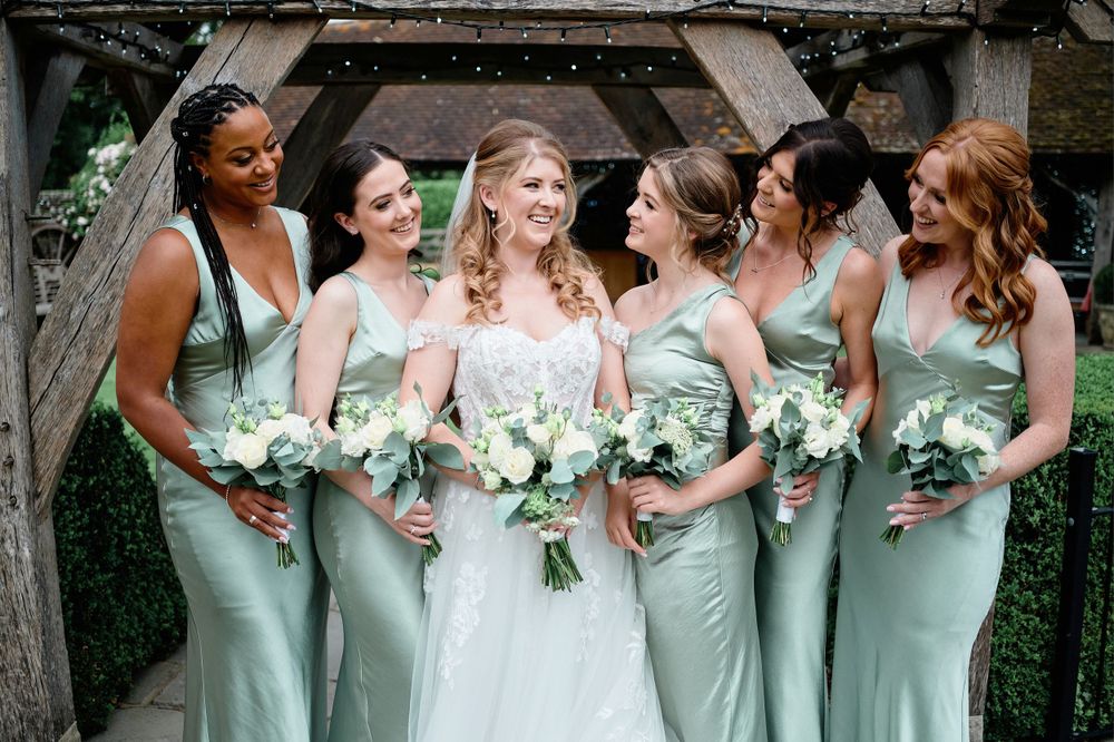 Bridesmaids wearing sage green dresses hold white bouquets while posing together outdoors.