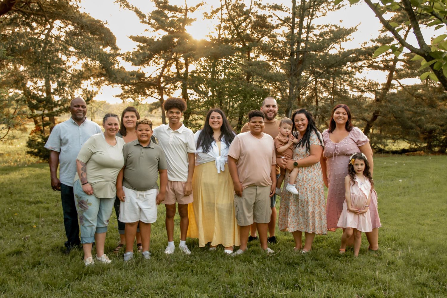 Large multigenerational family portrait gathered together on green lawn at golden hour sunset.