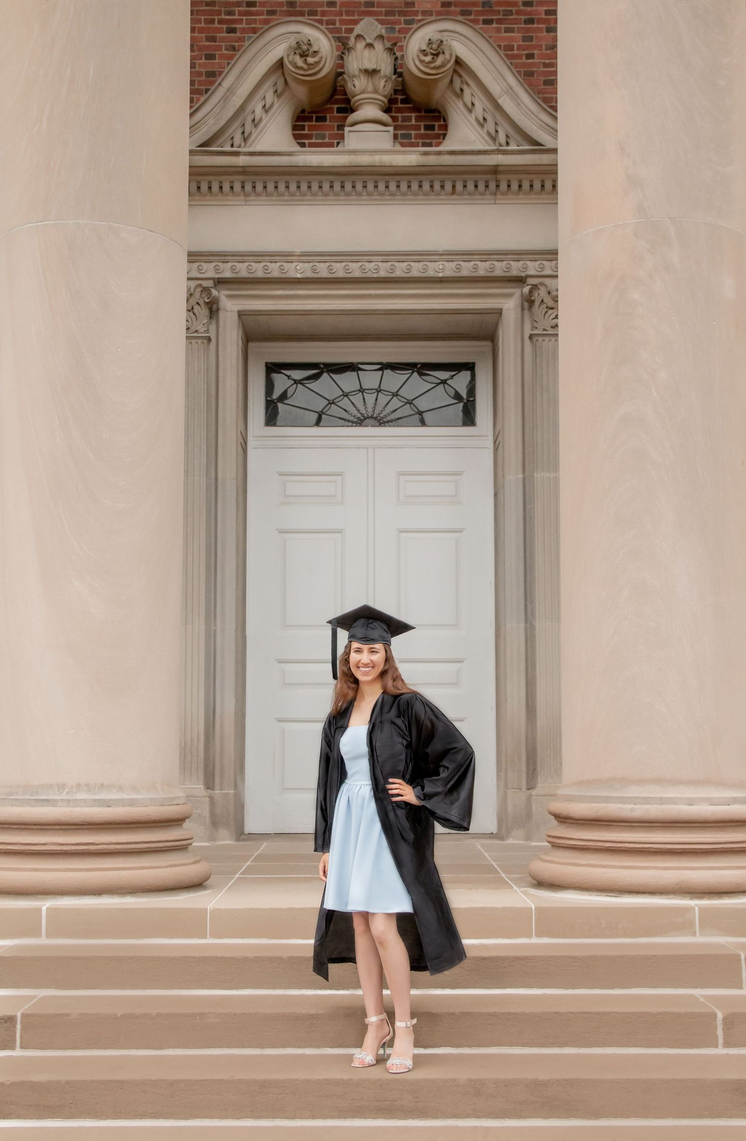 Graduate in cap and gown standing on steps before an ornate building entrance after ceremony.