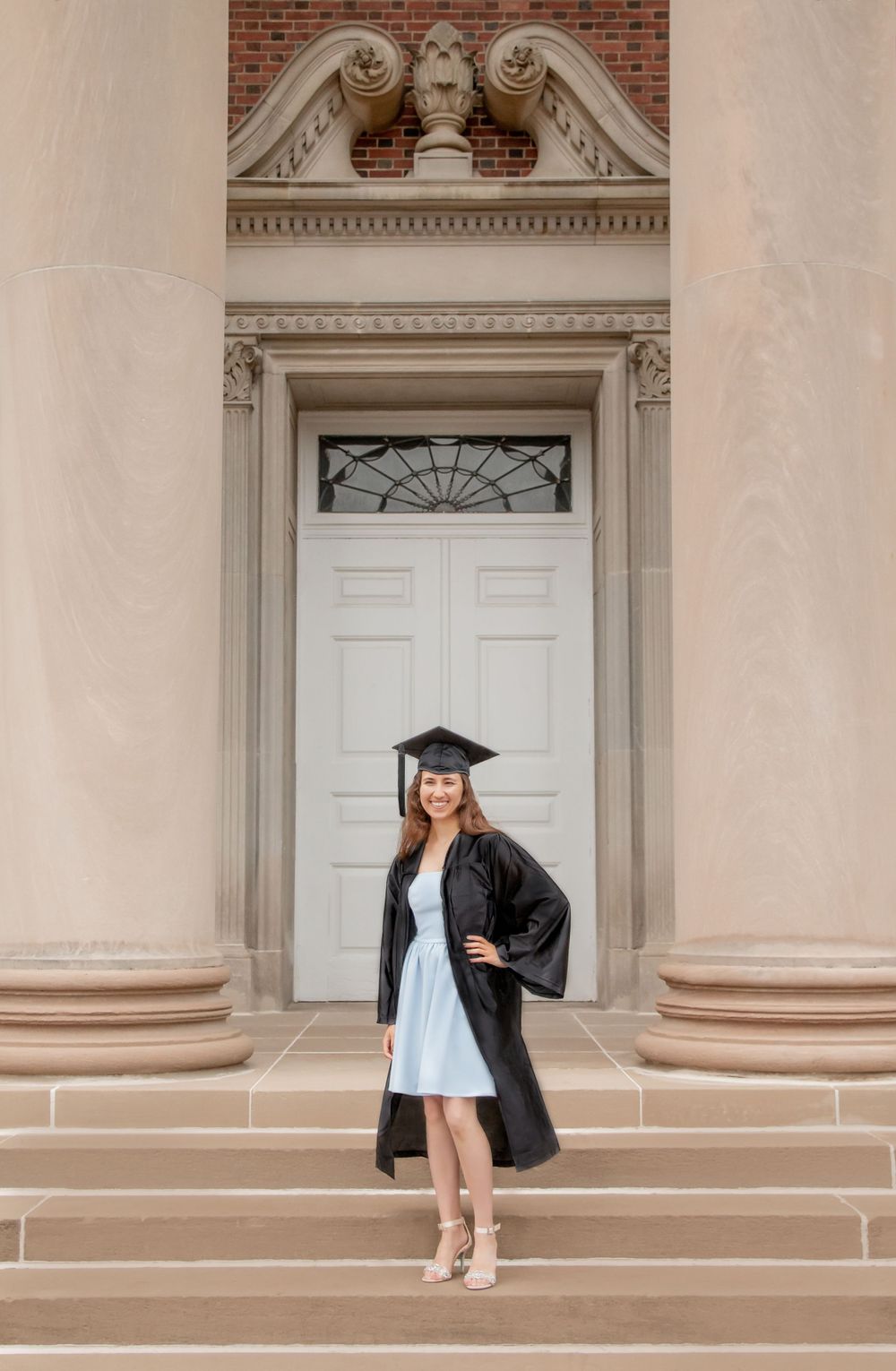 Graduate in cap and gown standing on steps before an ornate building entrance after ceremony.