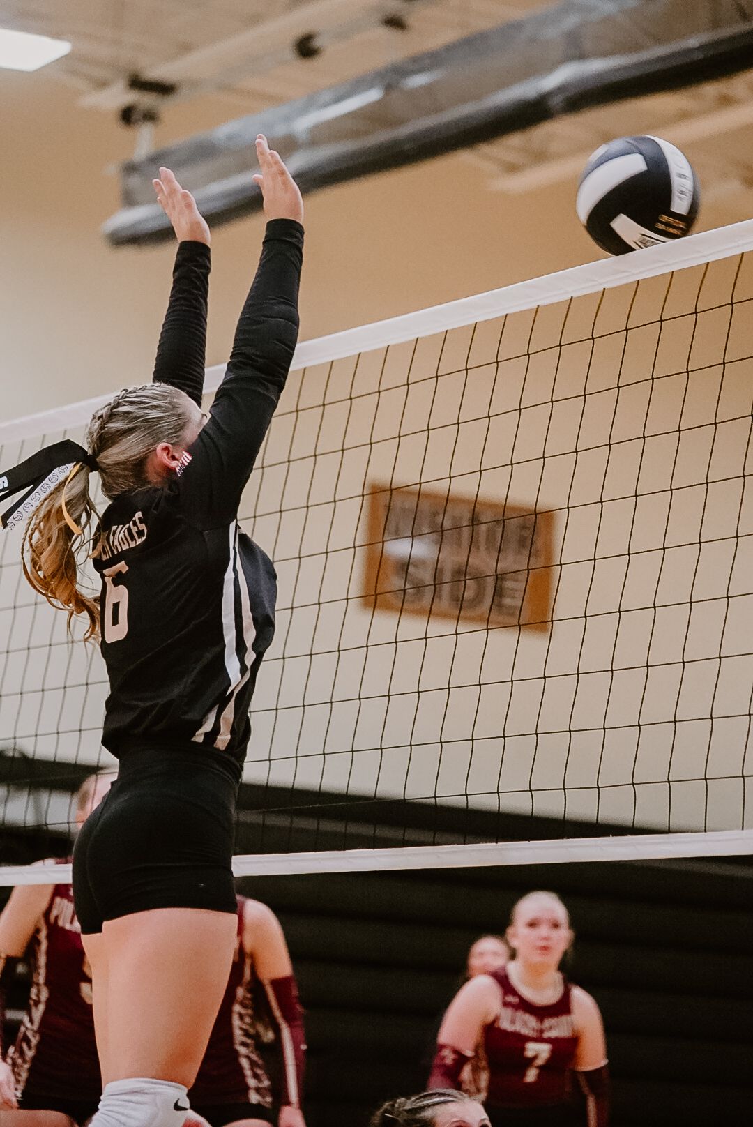 Volleyball players in black jerseys jumping to block at the net during a match.
