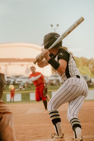 Female softball batter in pinstripe uniform ready to swing at incoming pitch during a sunny outdoor game.