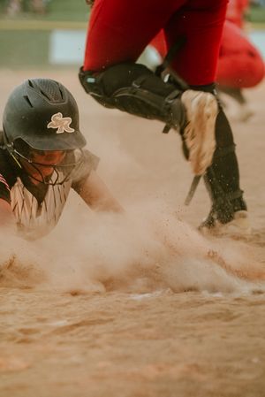 Softball player sliding into base in a cloud of dust while catcher attempts a tag during an intense game.