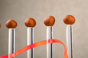Five chrome mallets with round brown heads and an orange ribbon weaving between them on a gray background.