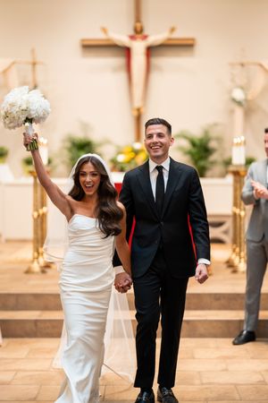 Happy couple exits church after wedding ceremony with celebratory gestures.