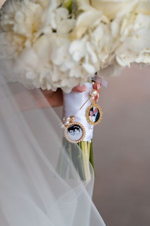 White bridal bouquet decorated with sentimental photo charms and mementos.