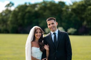 Wedding couple posing together on sunny green field with trees in background.