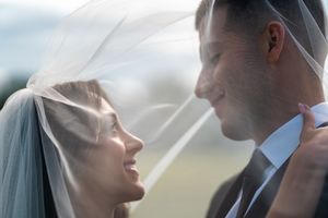 Intimate wedding portraits captured through flowing veil against blue sky.