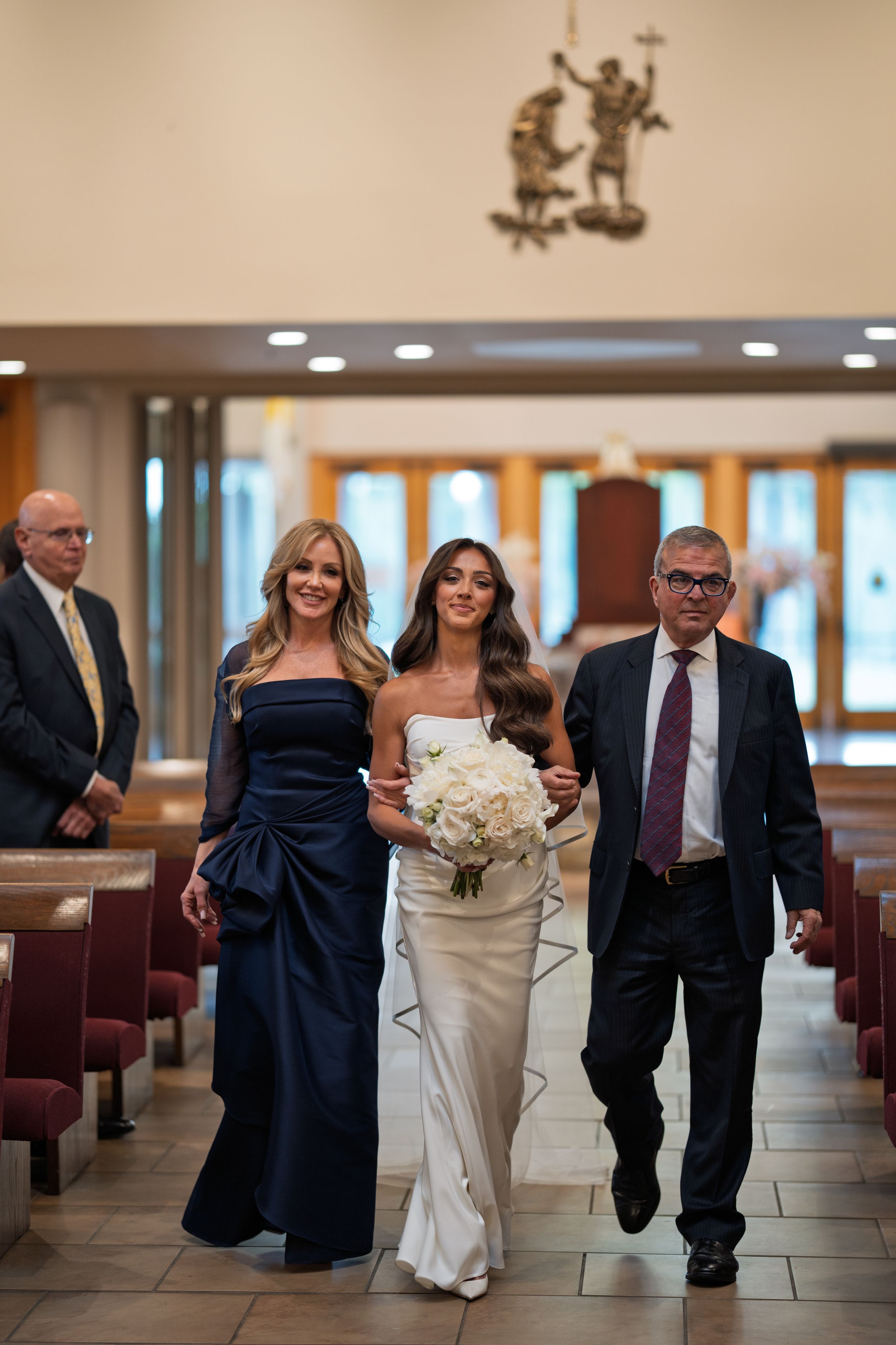 Wedding party walks down a hallway with the bride in white holding a bouquet.