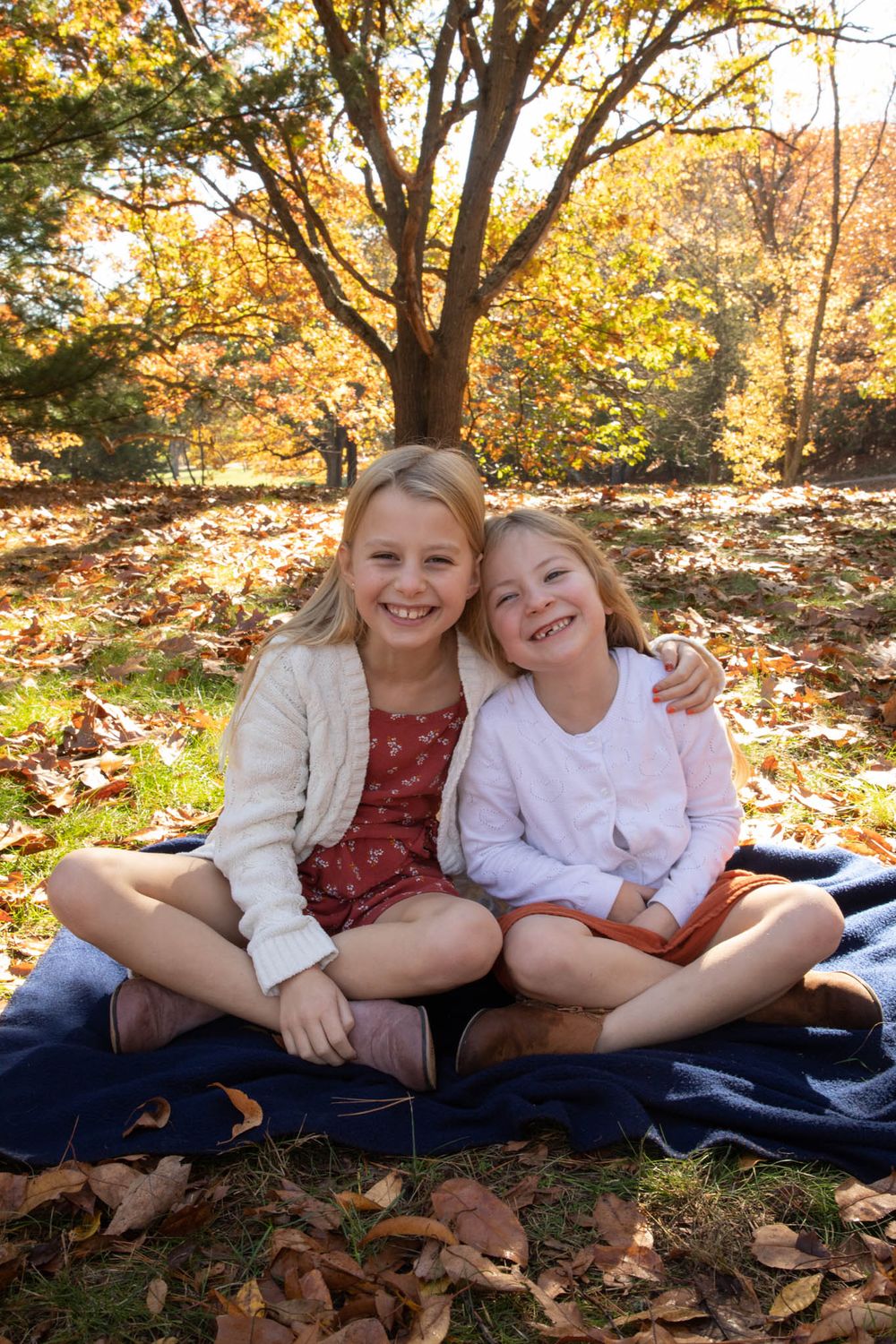 Children lounging on blanket among fallen autumn leaves during outdoor photo session.