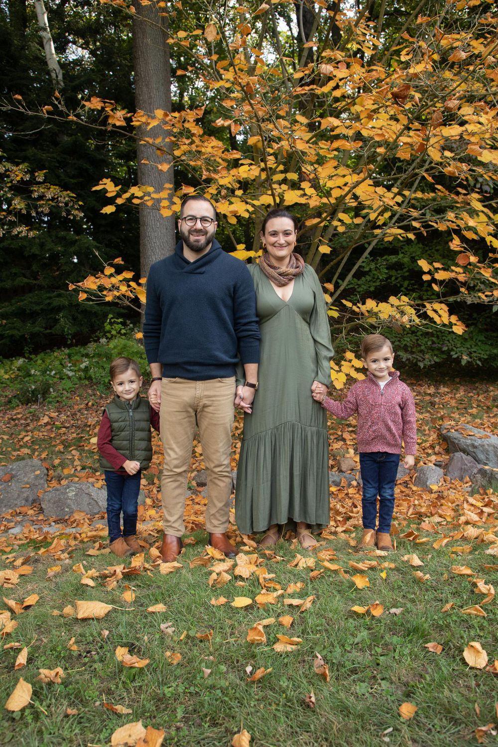 A family of four poses for an autumn portrait surrounded by golden leaves and trees.