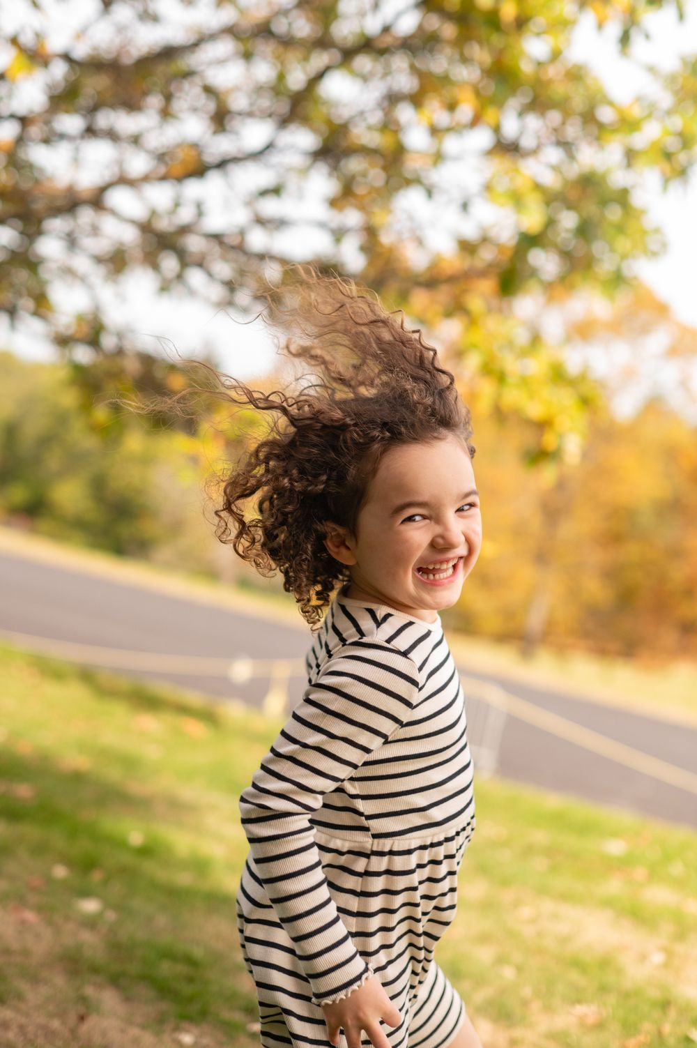A person wearing a striped sweater twirls joyfully outdoors on an autumn day with golden sunlight in the background.