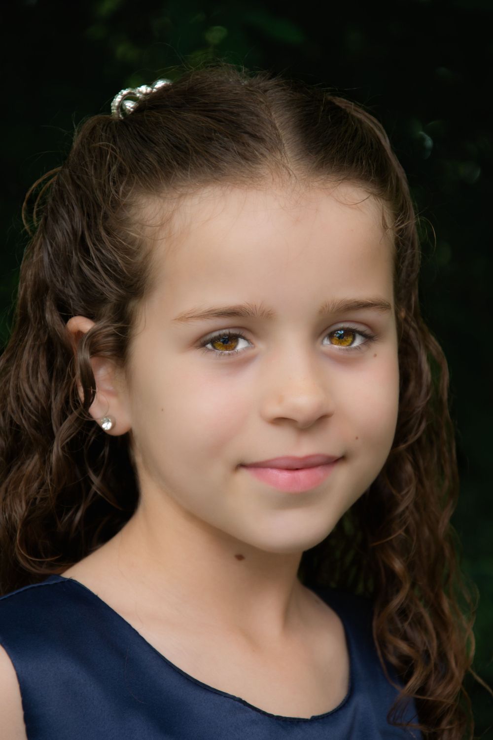Portrait with curly hair and delicate pearl hair accessories against dark background.