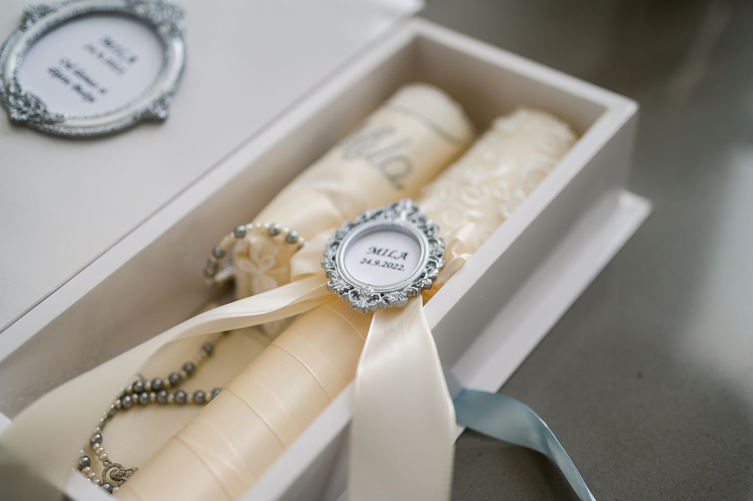 Decorated white unity candles in an elegant box with ribbon and ornate medallion detail.