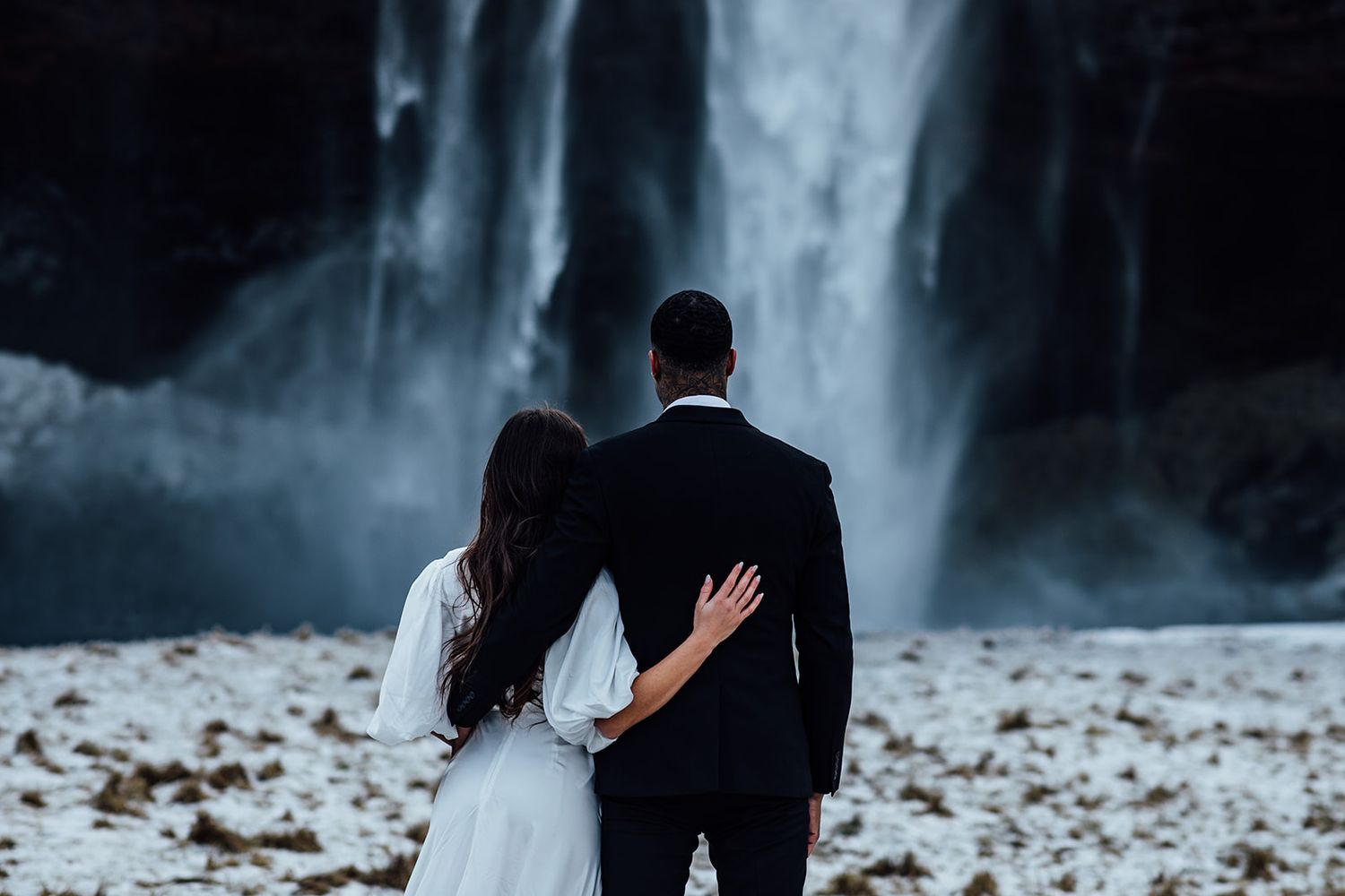 Newlyweds walk through golden field at sunset creating silhouettes against bright sky.
