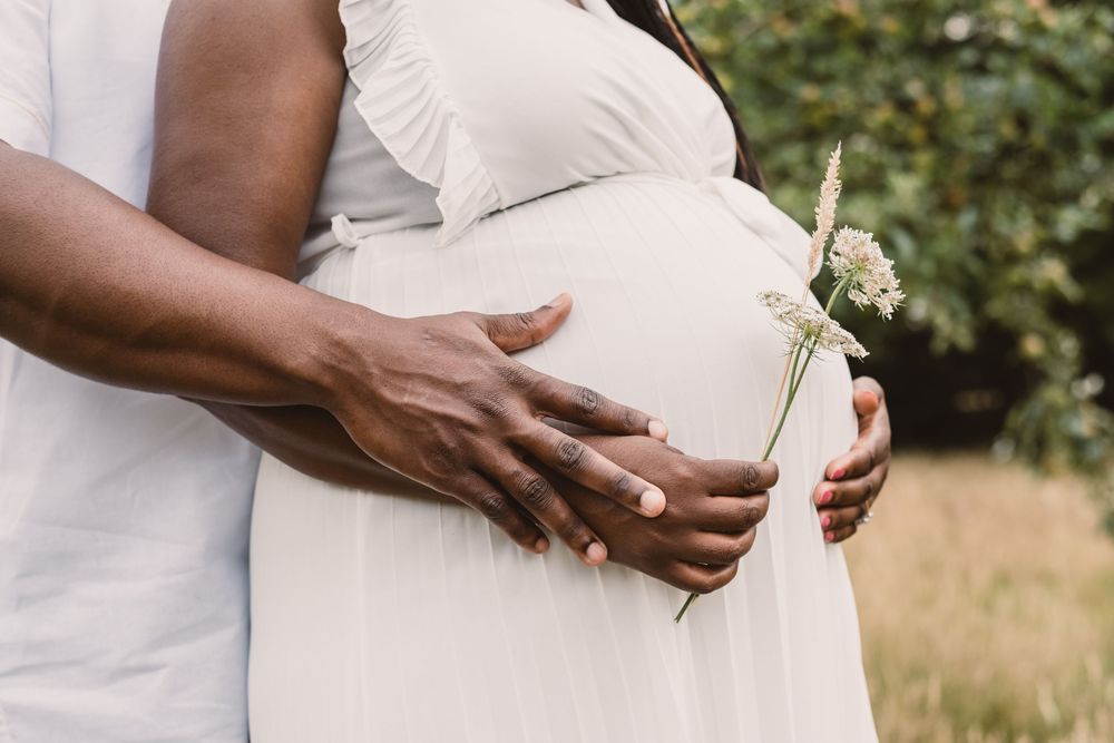 A close up image of a couple's hands on the woman's pregnant belly in a sunlit outdoor setting.