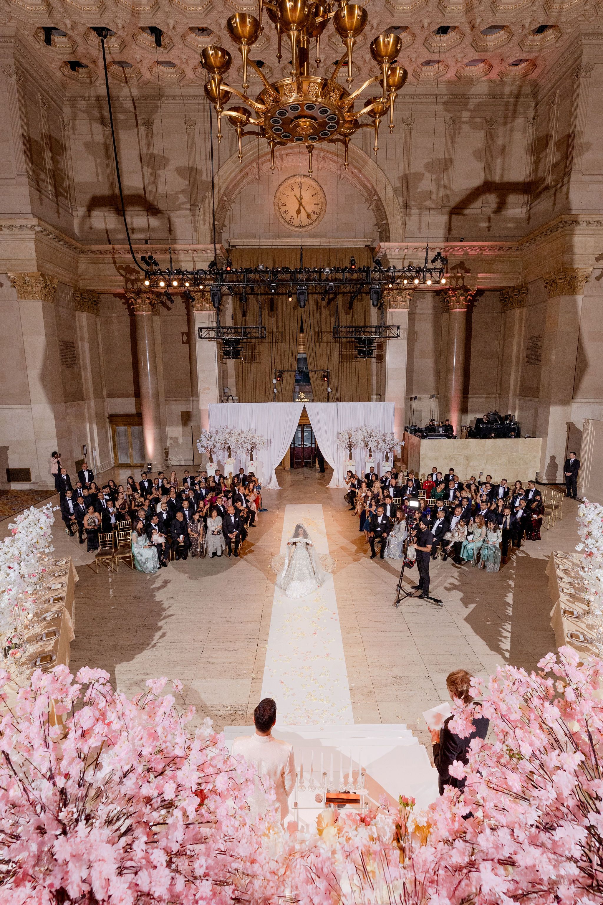 An aerial view of an elegant wedding ceremony in a grand ballroom with pink floral decorations.