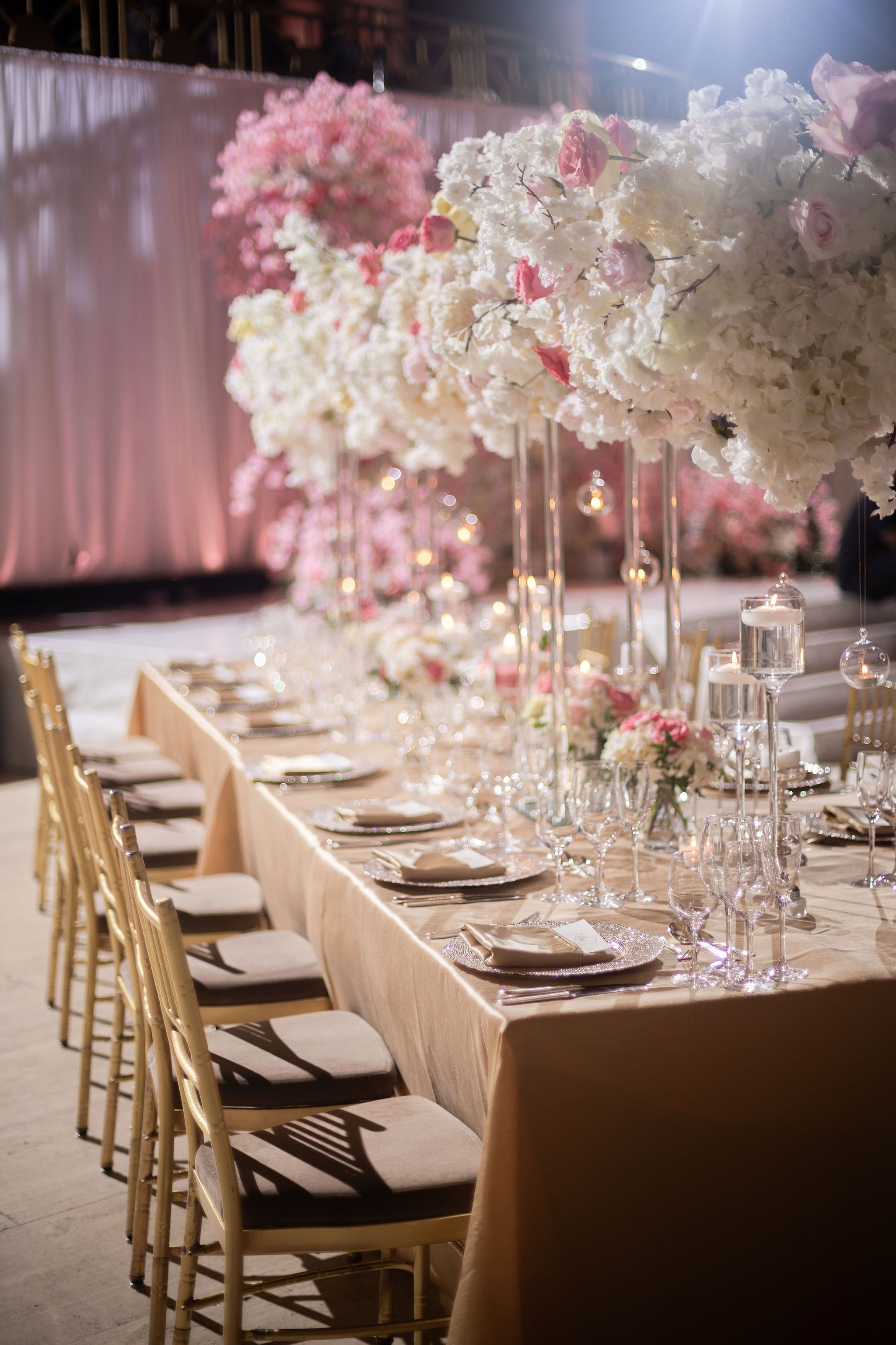 Long dining table with tall pink and white floral arrangements and gold chairs.