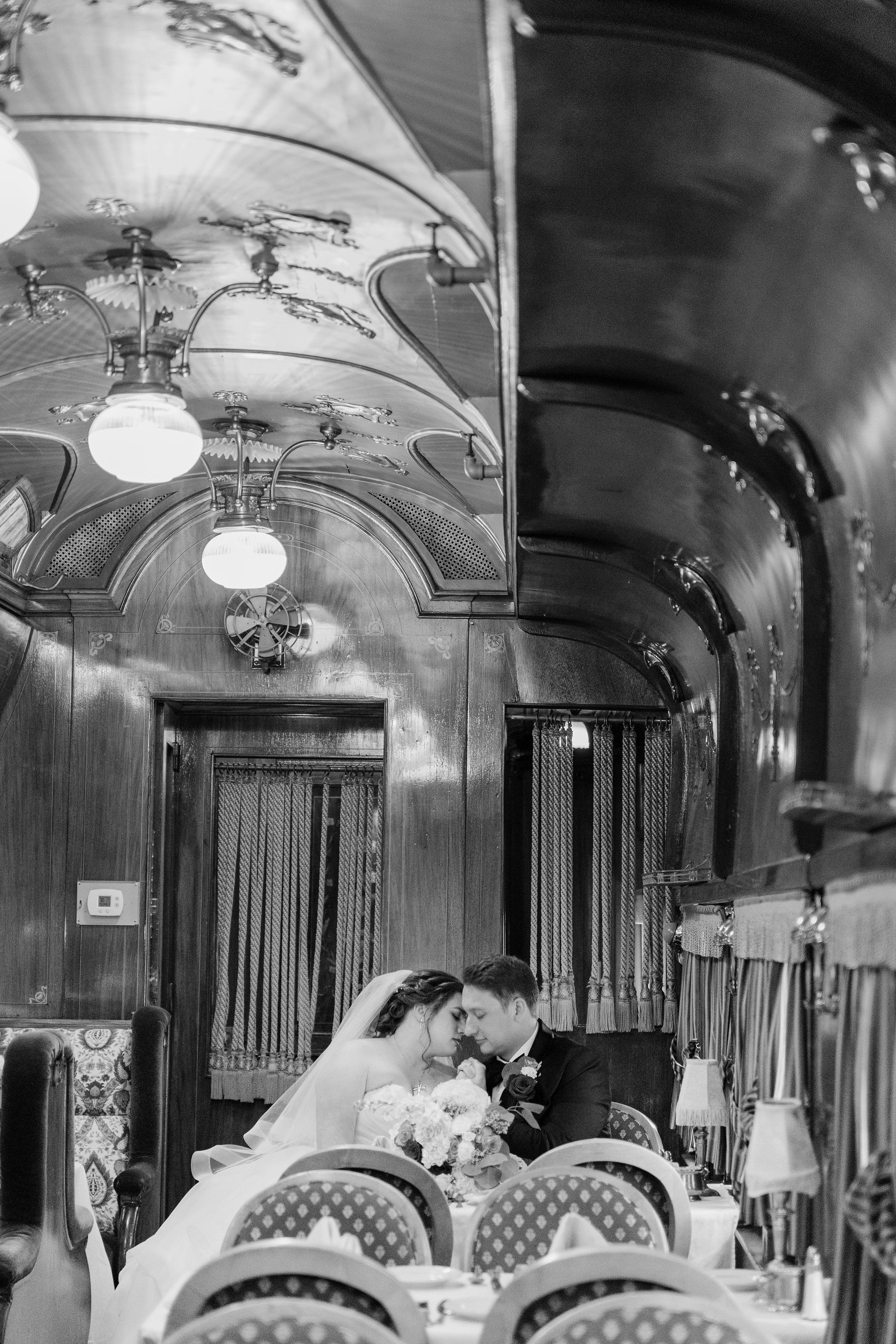 A vintage black and white wedding photo captured inside an elegant train car interior.