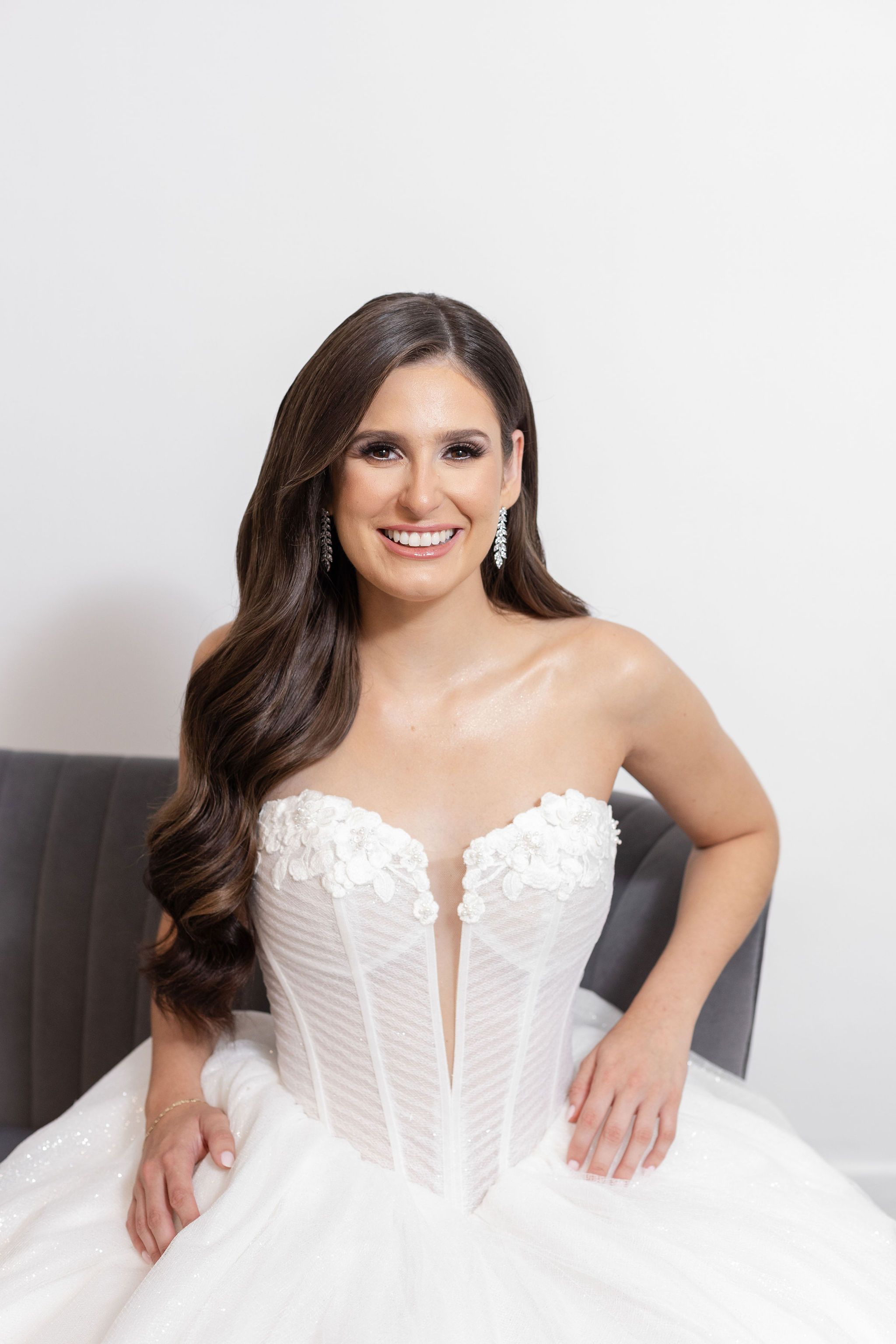 Person sitting wearing strapless white wedding gown with lace details on gray couch.