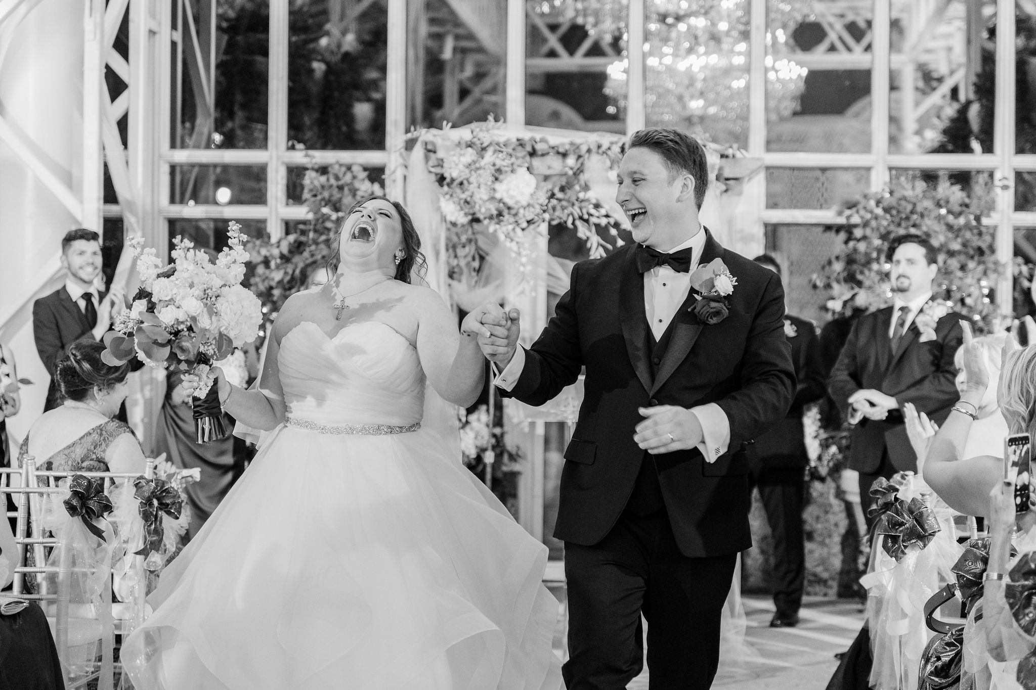 Couple sharing a laughter-filled moment during their wedding ceremony in a glass conservatory.