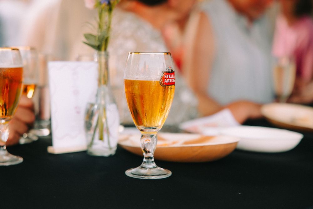 A Stella Artois beer in a stemmed glass on a black tablecloth at an elegant wedding reception dinner.