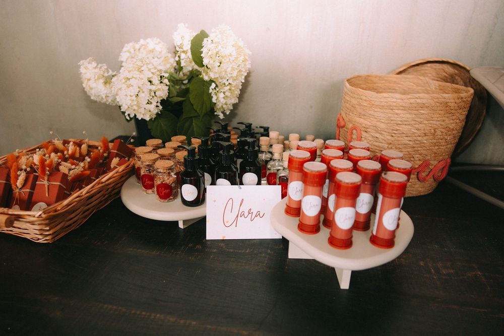 Wedding favor display table with red candles, mini jars, and white flowers next to a wicker basket.