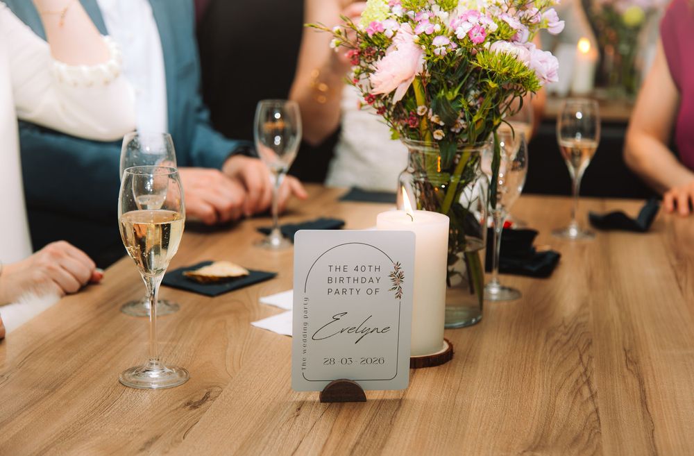 Elegant 40th birthday party table setting with champagne flutes, floral centerpiece, candle, and personalized party sign.