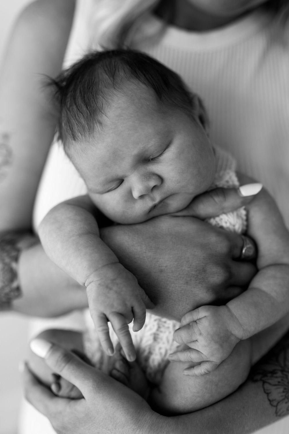 Peaceful black and white portrait of a sleeping newborn baby nestled in protective arms.