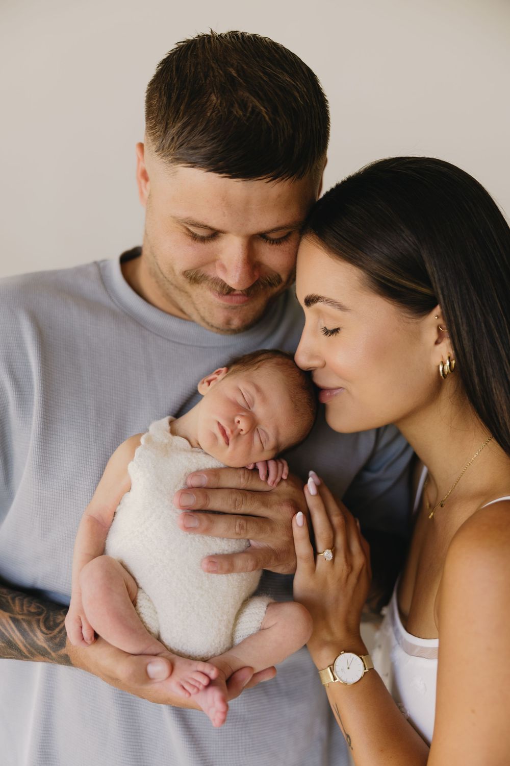 A tender series of photos showing parents sharing intimate moments with their newborn baby in a bright studio setting.
