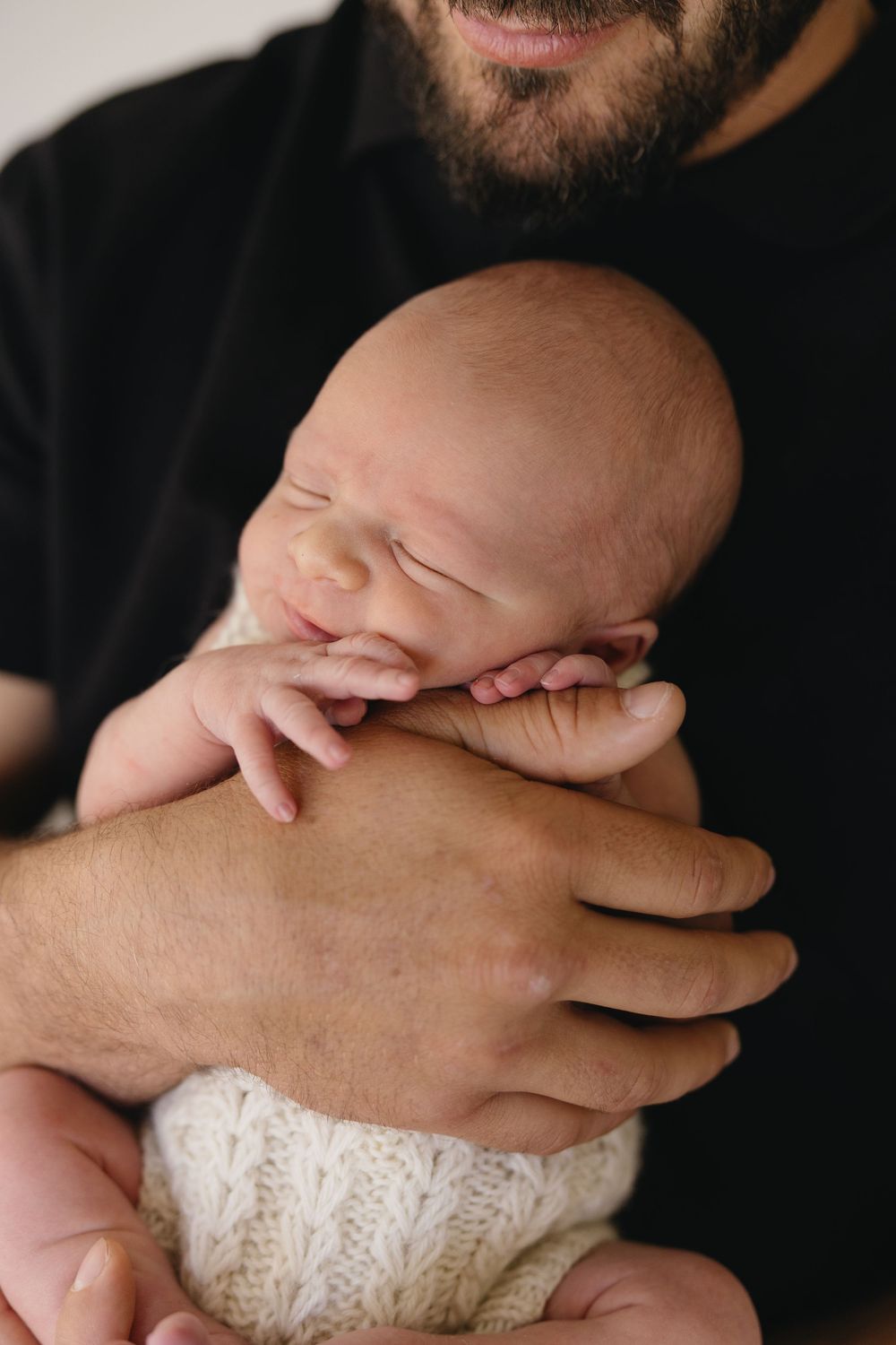 A series of close-up shots showing hands holding and caressing a baby wrapped in a white knit blanket.