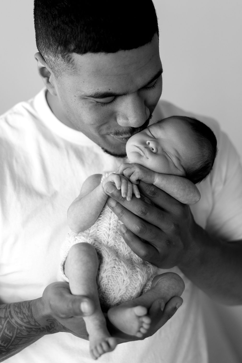 A parent tenderly kisses their newborn baby's feet in a series of black and white photos.