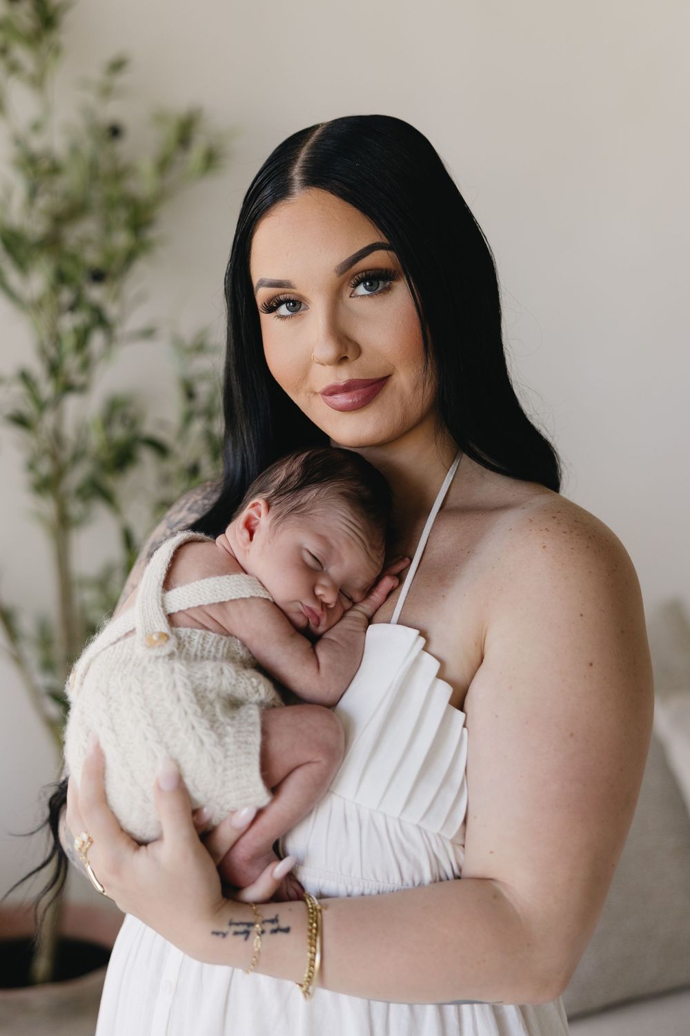 A mother in a white top holds and embraces a sleeping newborn baby in a series of intimate portraits.