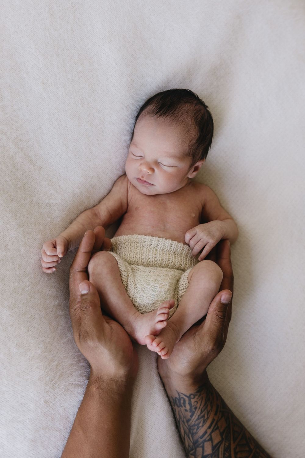 A newborn baby lies peacefully on white fabric while gentle hands cradle their small body in a series of tender poses.