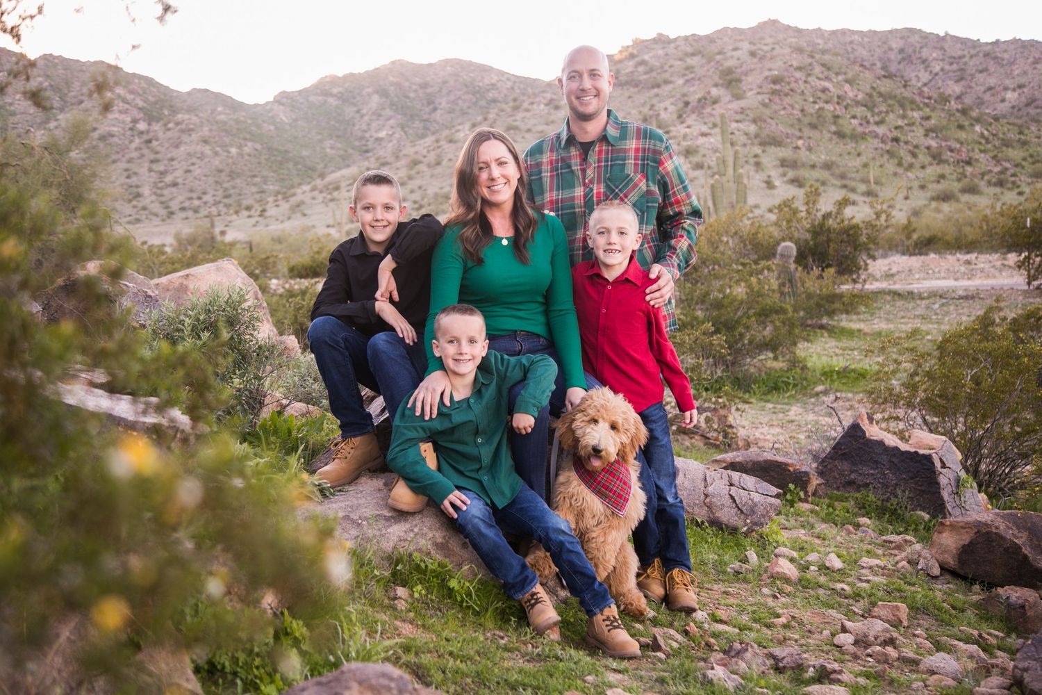 Family of five with golden retriever poses on rocks in desert mountain landscape.