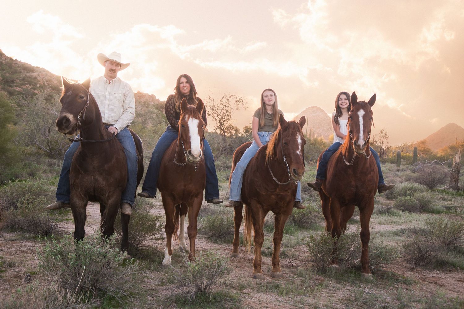 Family of four rides horses through desert terrain with mountains at golden hour.