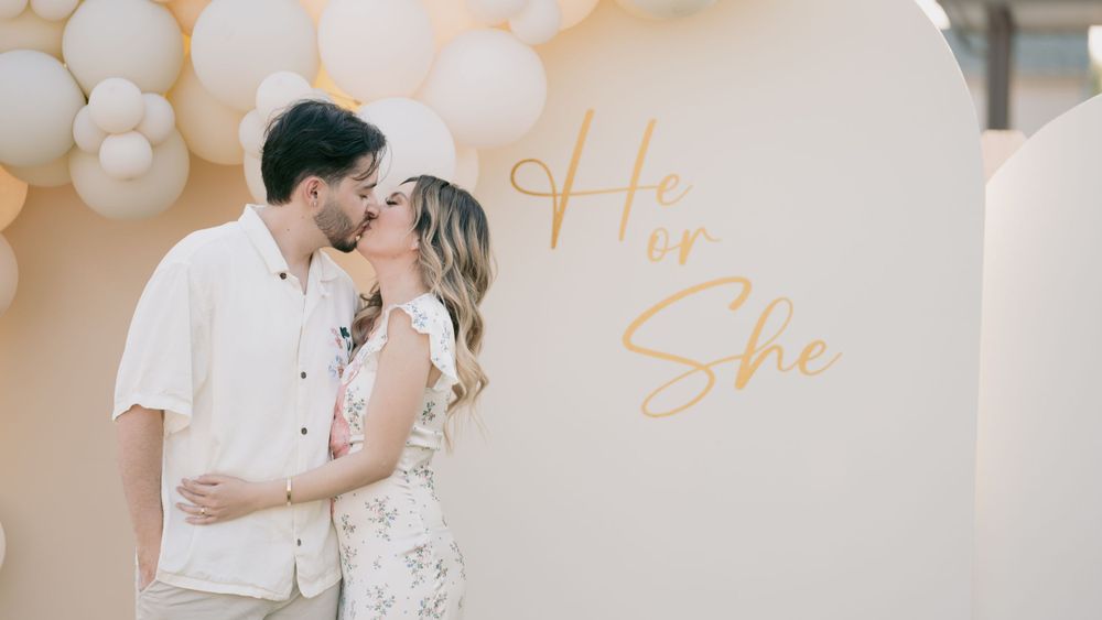 Couple sharing intimate moment against white balloon wall with gold 'She Said' text.