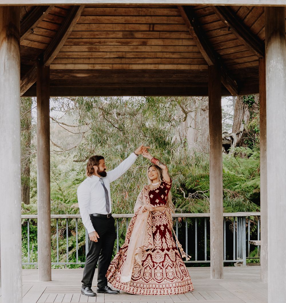 A couple in formal attire dancing together under a wooden gazebo with lush greenery in the background.