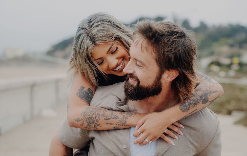 A joyful couple embrace outdoors with visible tattoos and warm sunlight creating an intimate candid moment.