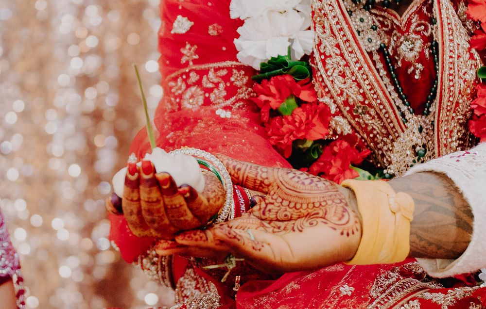 Traditional bridal hands adorned with intricate henna designs holding red flowers.