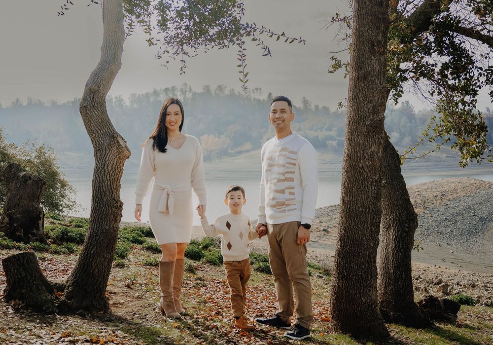 Family in white and beige outfits poses together on hillside with scenic mountain view.