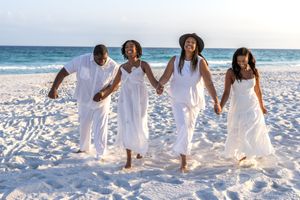 Happy family in white outfits holding hands and running on a sunny beach together.