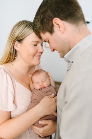 mom and dad holding newborn baby upright and swaddled