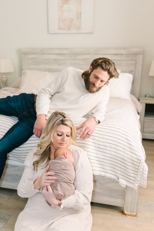 mom sitting with newborn baby and dad sitting on bed adoring them