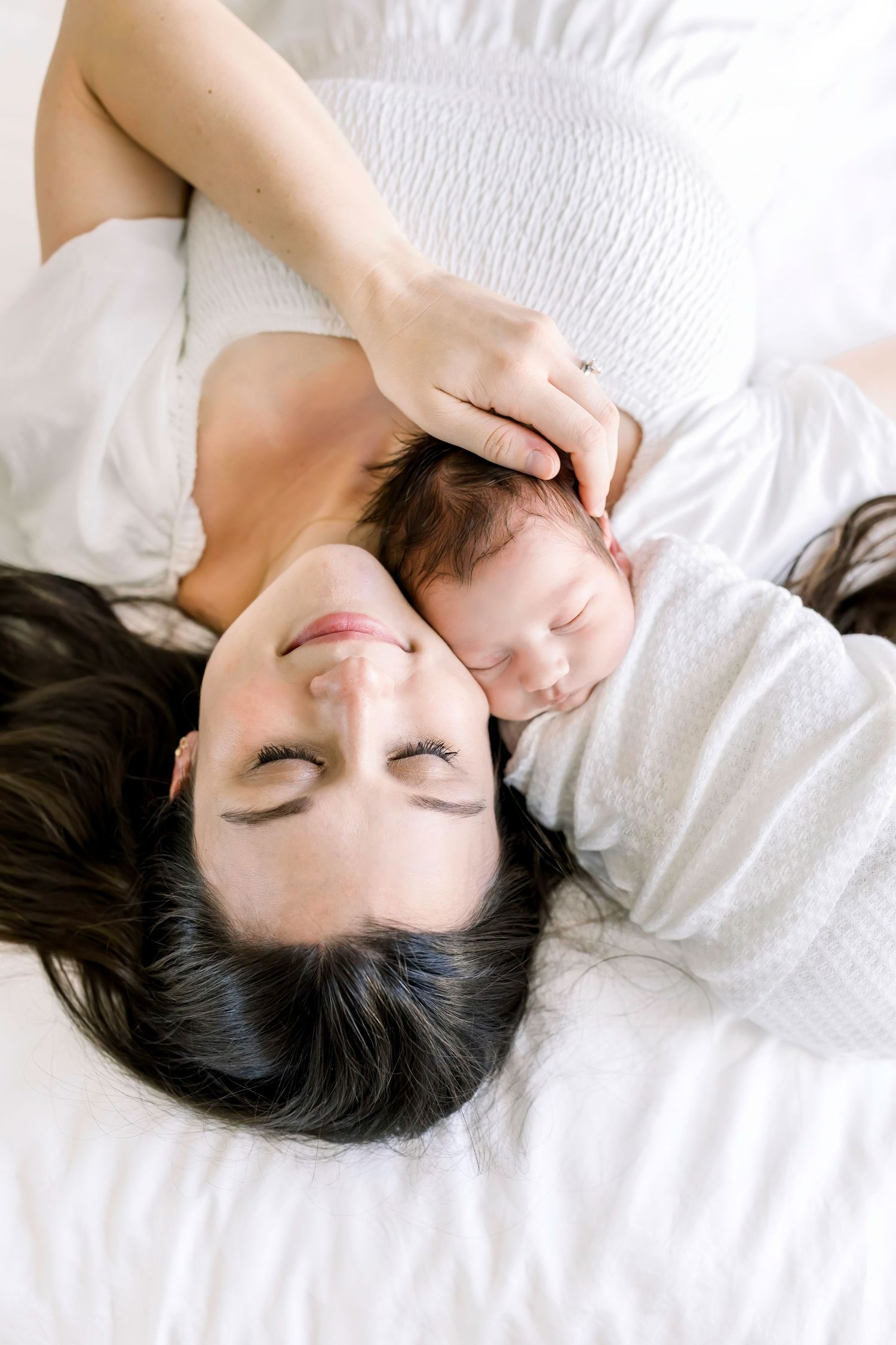 A tender moment between mother and baby laying on white bedding.