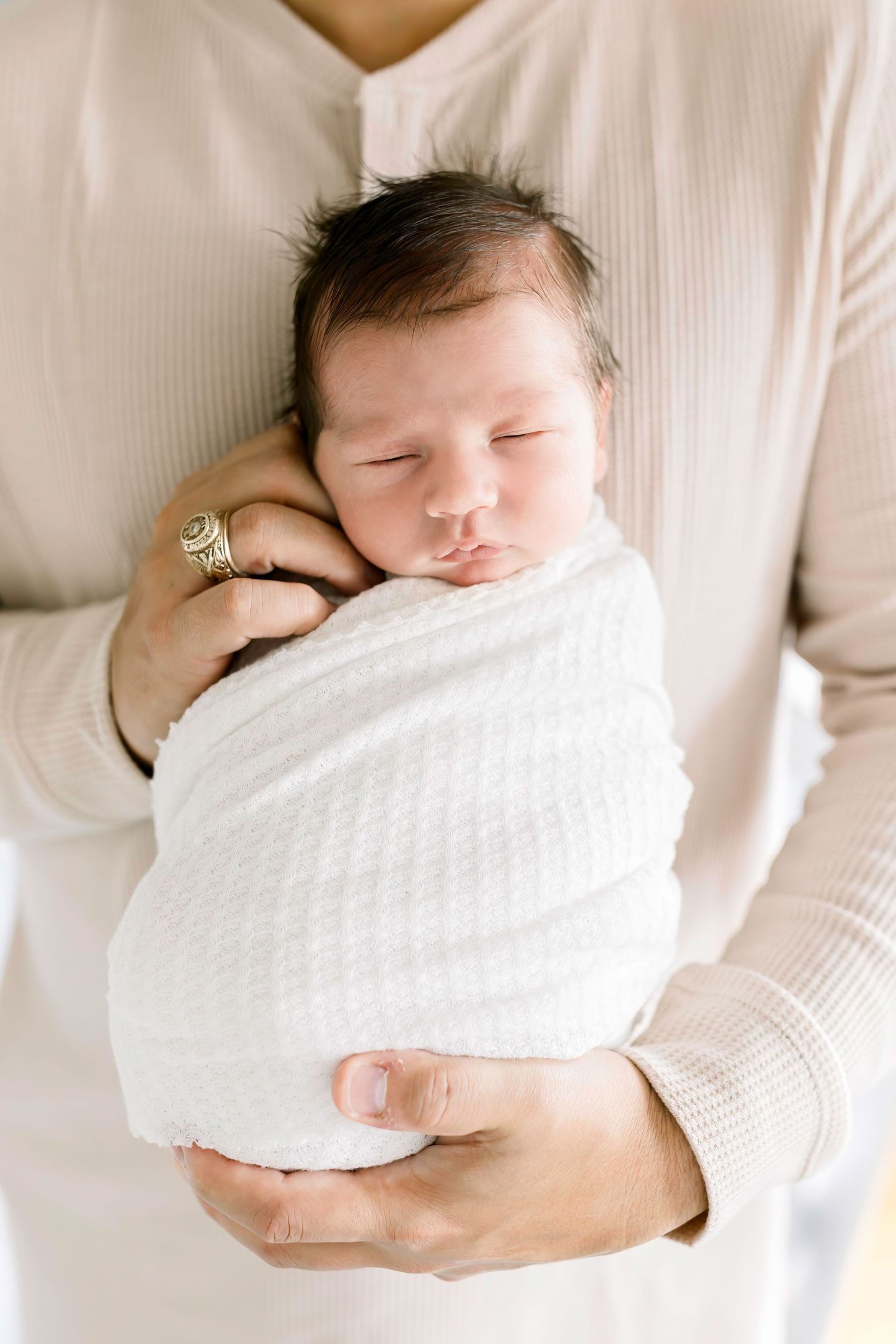 Sleeping newborn swaddled in white blanket being held against white sweater.