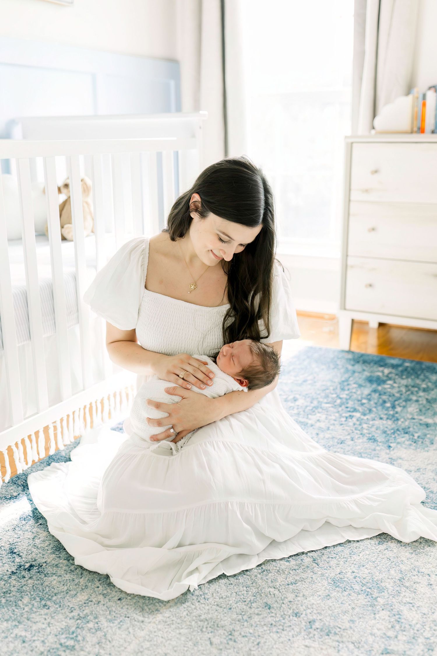 Peaceful nursery scene with mother in white dress sitting on floor with newborn.